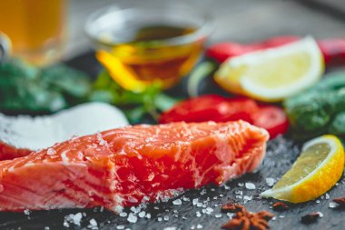 Çiğ somon fileto ve karanlık arka planda yemek pişirmek için malzemeler.