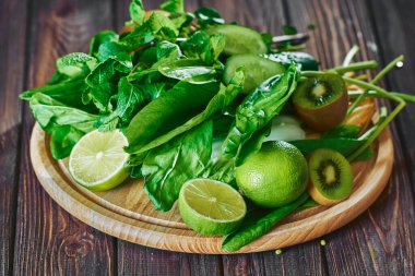 Taş tahtadaki malzemelerle harmanlanmış yeşil smoothie, ahşap masa.