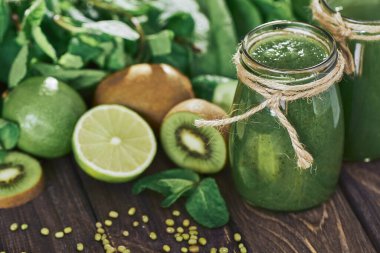 Taş tahtadaki malzemelerle harmanlanmış yeşil smoothie, ahşap masa.