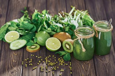 Taş tahtadaki malzemelerle harmanlanmış yeşil smoothie, ahşap masa.