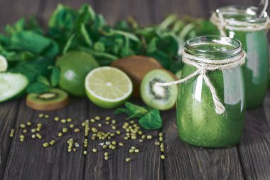 Taş tahtadaki malzemelerle harmanlanmış yeşil smoothie, ahşap masa.