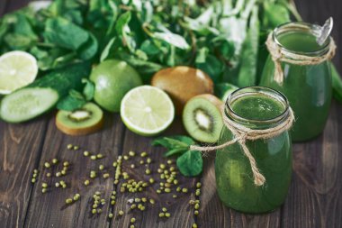 Taş tahtadaki malzemelerle harmanlanmış yeşil smoothie, ahşap masa.