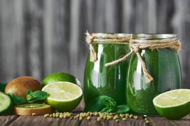 Taş tahtadaki malzemelerle harmanlanmış yeşil smoothie, ahşap masa.