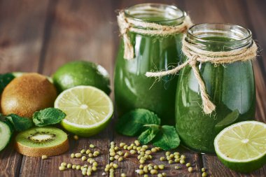 Taş tahtadaki malzemelerle harmanlanmış yeşil smoothie, ahşap masa.