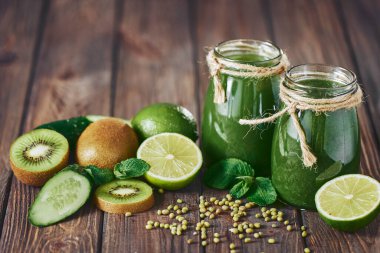 Taş tahtadaki malzemelerle harmanlanmış yeşil smoothie, ahşap masa.