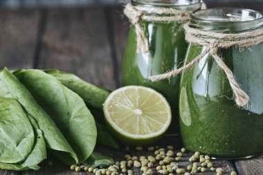 Taş tahtadaki malzemelerle harmanlanmış yeşil smoothie, ahşap masa.