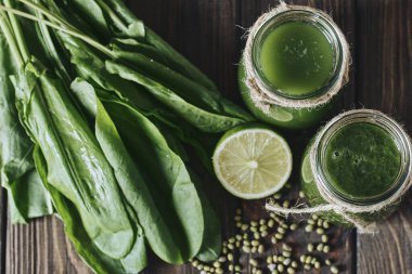 Taş tahtadaki malzemelerle harmanlanmış yeşil smoothie, ahşap masa.