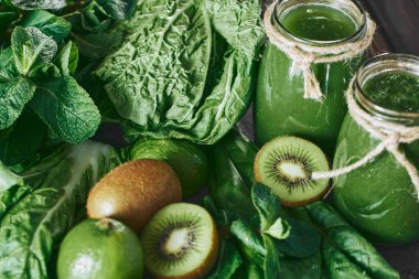 Taş tahtadaki malzemelerle harmanlanmış yeşil smoothie, ahşap masa.