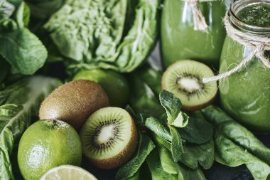 Taş tahtadaki malzemelerle harmanlanmış yeşil smoothie, ahşap masa.