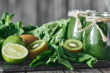 Taş tahtadaki malzemelerle harmanlanmış yeşil smoothie, ahşap masa.
