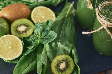 Taş tahtadaki malzemelerle harmanlanmış yeşil smoothie, ahşap masa.