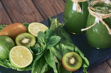 Taş tahtadaki malzemelerle harmanlanmış yeşil smoothie, ahşap masa.