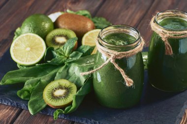 Taş tahtadaki malzemelerle harmanlanmış yeşil smoothie, ahşap masa.