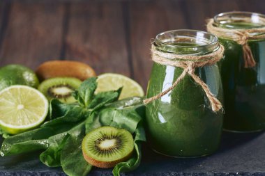 Taş tahtadaki malzemelerle harmanlanmış yeşil smoothie, ahşap masa.