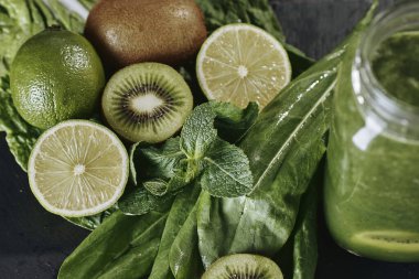 Taş tahtadaki malzemelerle harmanlanmış yeşil smoothie, ahşap masa.