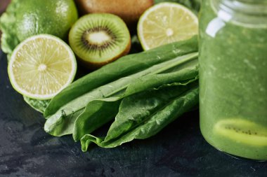 Taş tahtadaki malzemelerle harmanlanmış yeşil smoothie, ahşap masa.