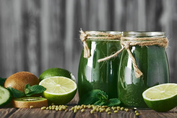 Taş tahtadaki malzemelerle harmanlanmış yeşil smoothie, ahşap masa.