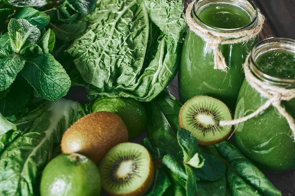 Taş tahtadaki malzemelerle harmanlanmış yeşil smoothie, ahşap masa.