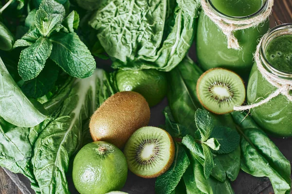 Taş tahtadaki malzemelerle harmanlanmış yeşil smoothie, ahşap masa.