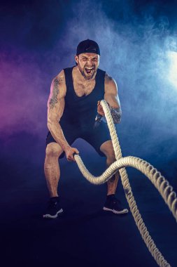 Sakallı sporcu görünüşlü vücut bulucu savaş halatıyla çalışıyor.