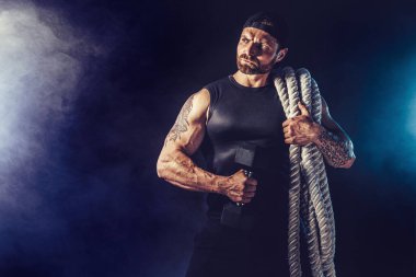 Sakallı atletik görünüşlü vücut bulucu elinde savaş ipi ve iğnesi tutuyor.