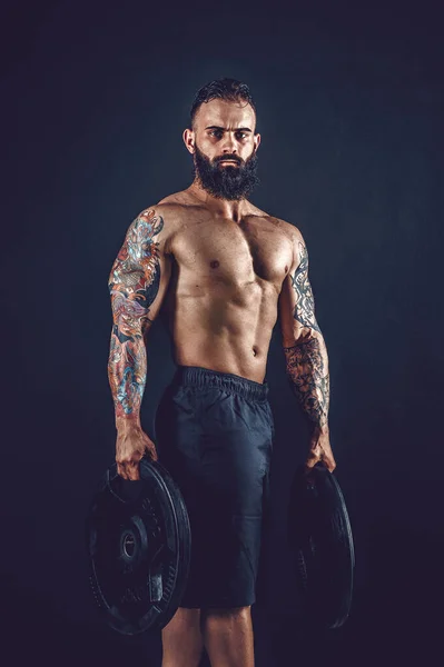 Студійний портрет без сорочки татуйованого бородатого чоловіка тримає гантелі — стокове фото