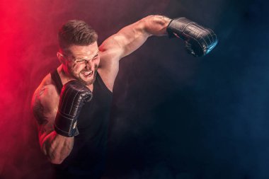 Sakallı sporcu Muay Thai boksörü siyah fanilalı ve boks eldivenli siyah arka planda dumanla dövüşüyor..