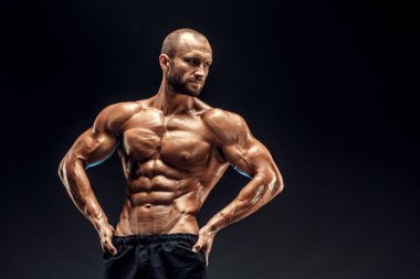 Mükemmel karın kasları, omuzları, pazıları, kol ve göğsü olan güçlü bir adam. Vücut geliştiren üstsüz siyah arka plan üzerinde kaslarını esnetiyor.