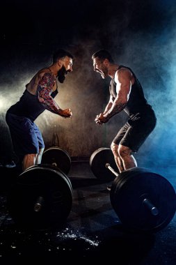İki sakallı, kaslı adam birbirine bakar ve spor salonunda bağırır.