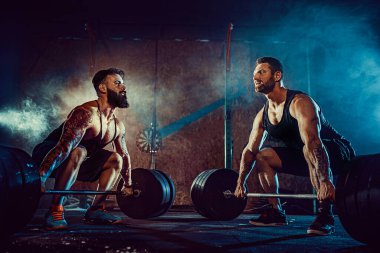 İki kaslı sakallı sporcu spor salonunda antrenman yapıyor.