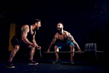 İki kaslı sakallı sporcu spor salonunda antrenman yapıyor.