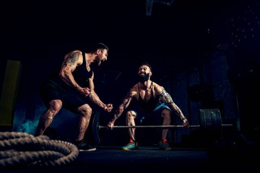 İki kaslı sakallı sporcu spor salonunda antrenman yapıyor.