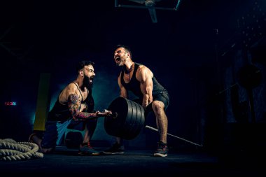 İki kaslı sakallı sporcu spor salonunda antrenman yapıyor.