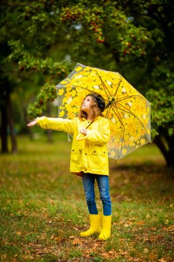 Sonbahar parkında lastik çizmeli, çok renkli şemsiyeli mutlu kız çocuğu.