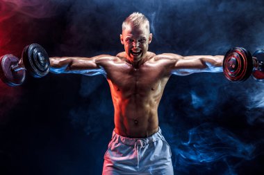 Konsantre olmuş kaslı adam dambılla egzersiz yapıyor.