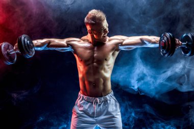 Konsantre olmuş kaslı adam dambılla egzersiz yapıyor.