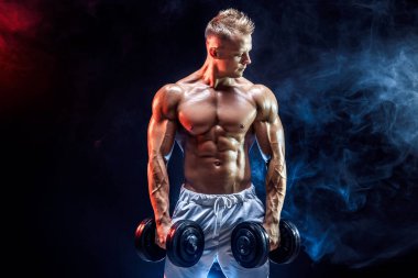 Stüdyoda dambıllarla pazı egzersizi yapan üstsüz bir adam.