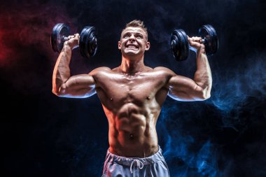 Konsantre olmuş kaslı adam dambılla egzersiz yapıyor.