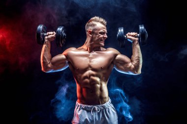 Konsantre olmuş kaslı adam dambılla egzersiz yapıyor.