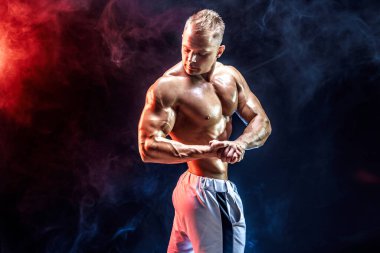 Stüdyoda dumanla poz veren yakışıklı güçlü vücut geliştirici.