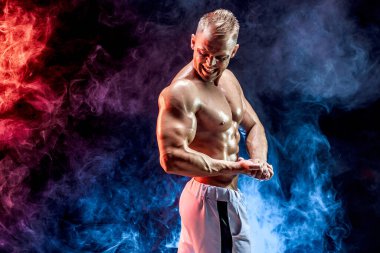 Stüdyoda dumanla poz veren yakışıklı güçlü vücut geliştirici.