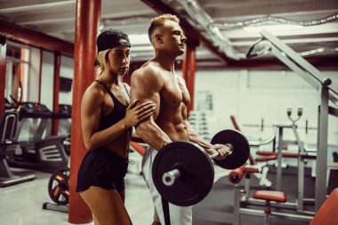 Genç bir adam ve bir kadın takımı dambıllarla antrenman yapıyor.