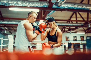 Boks ve nefsi müdafaada antrenörle egzersiz yapan genç bir kadın.