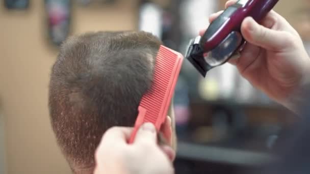 Omul din frizerie stă într-un fotoliu. Bărbierul își taie părul cu un trimer — Videoclip de stoc