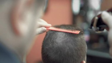 Berber dükkanındaki adam koltukta oturuyor. Berber saçını budayıcı ile kesiyor.