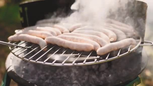 Kolbász grillsütőn, a szabadban. Grill. Grillezett étel sült és füstölt faszén grillezőben. Megfordítja a grillt finom kolbászokkal. — Stock videók