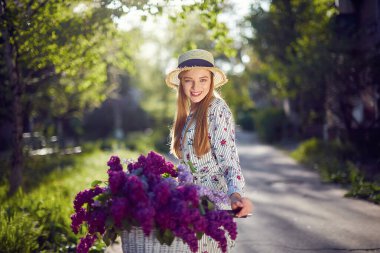 Şehrin arka planında klasik bisikletli ve çiçekli mutlu bir genç kızın portresi. Açık havada güneş ışığı altında.