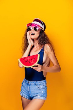 Şapkalı ve mayo giyen kadın bir karpuz dilimi tutuyor.