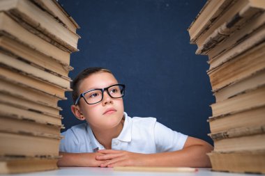 Gözlüklü zeki çocuk iki kitap yığınının arasında oturuyor ve bak.