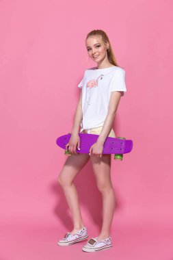 Pembe arka planda kaykayı olan neşeli bir genç kız.